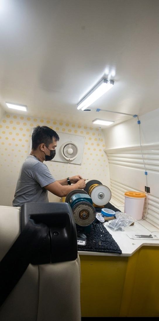 Technician sharpening scissors on a grinding wheel inside the Zahar van